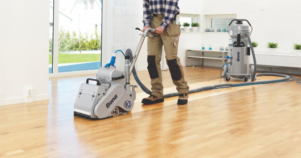 A professional using a Bona floor sander on a light hardwood floor with a dust containment unit in the background.