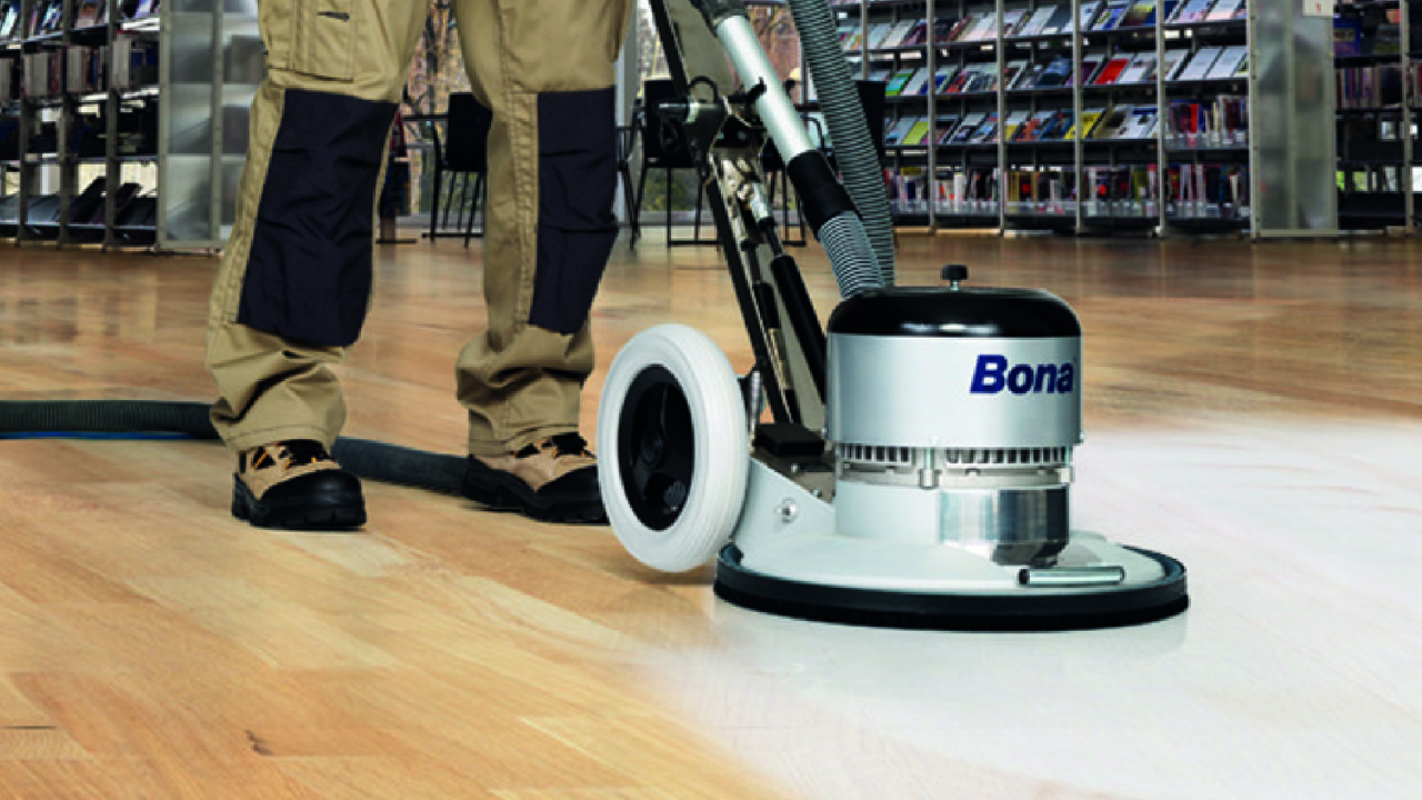 A floor technician operating a Bona sanding machine on a hardwood floor, illustrating the process of professional restoration.