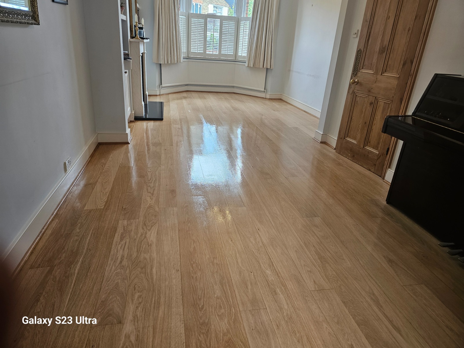 A bright, newly refinished oak living room floor with a high-gloss lacquer, showcasing the wood’s natural grain and reflective surface.