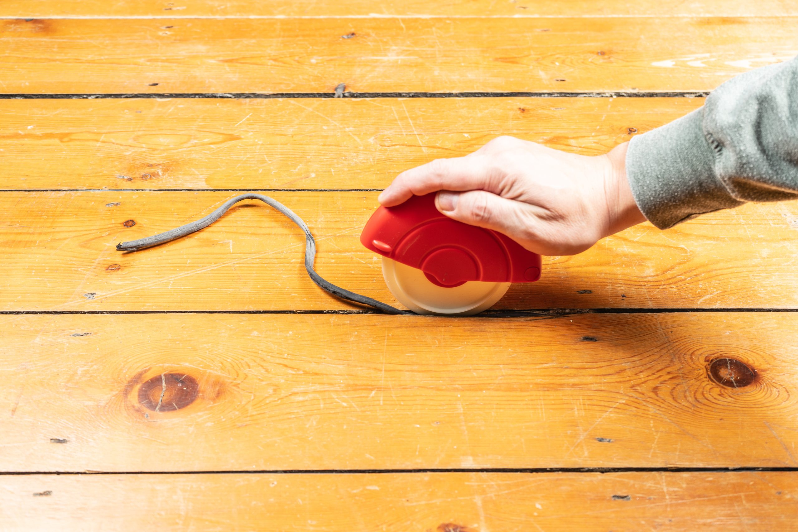 Southwark close-up of Victorian Pine floorboards as a technician uses a red roller tool to remove an old draught strip—prepping for Gap Strip Magic sealing before sanding and finishing.