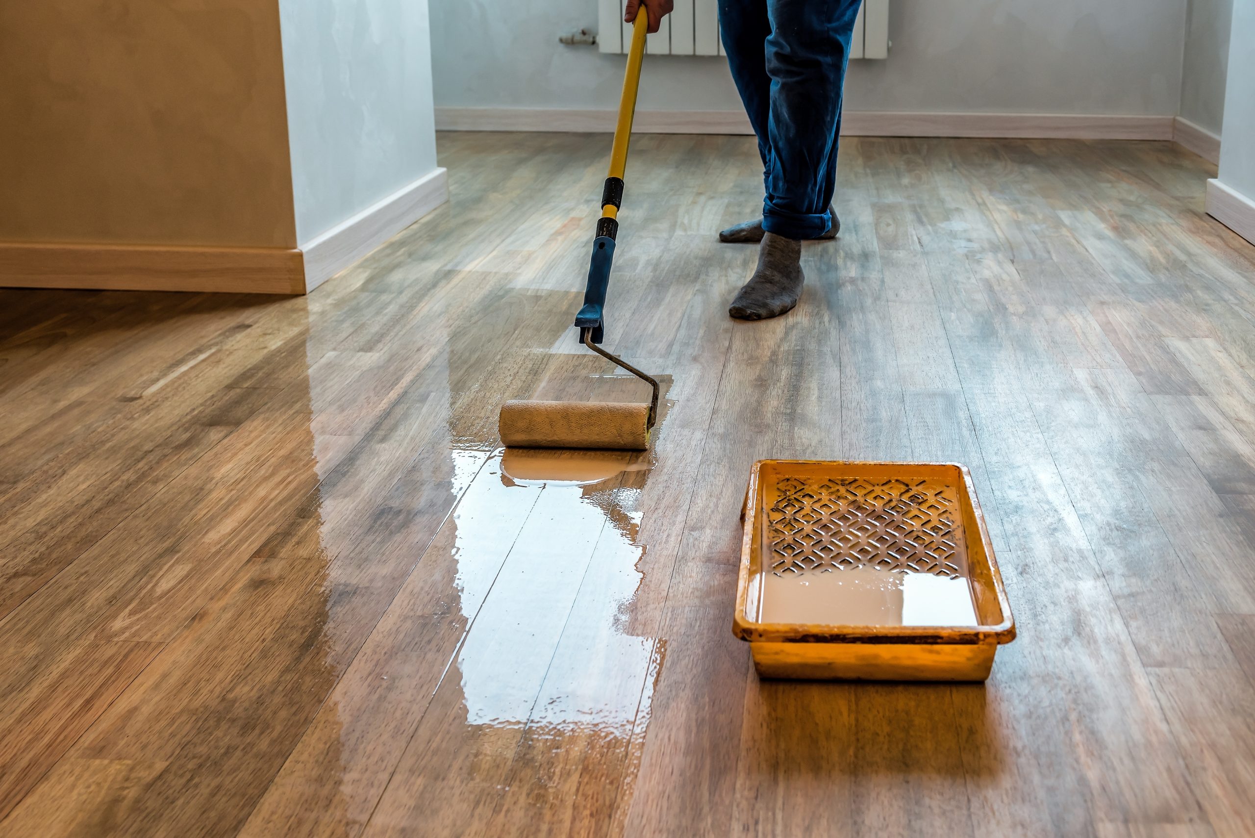 Southwark Walnut Hardwood Plank Floor being finished with a roller after Gap Strip Magic sealed the seams—clear lacquer creates a warm, even sheen.