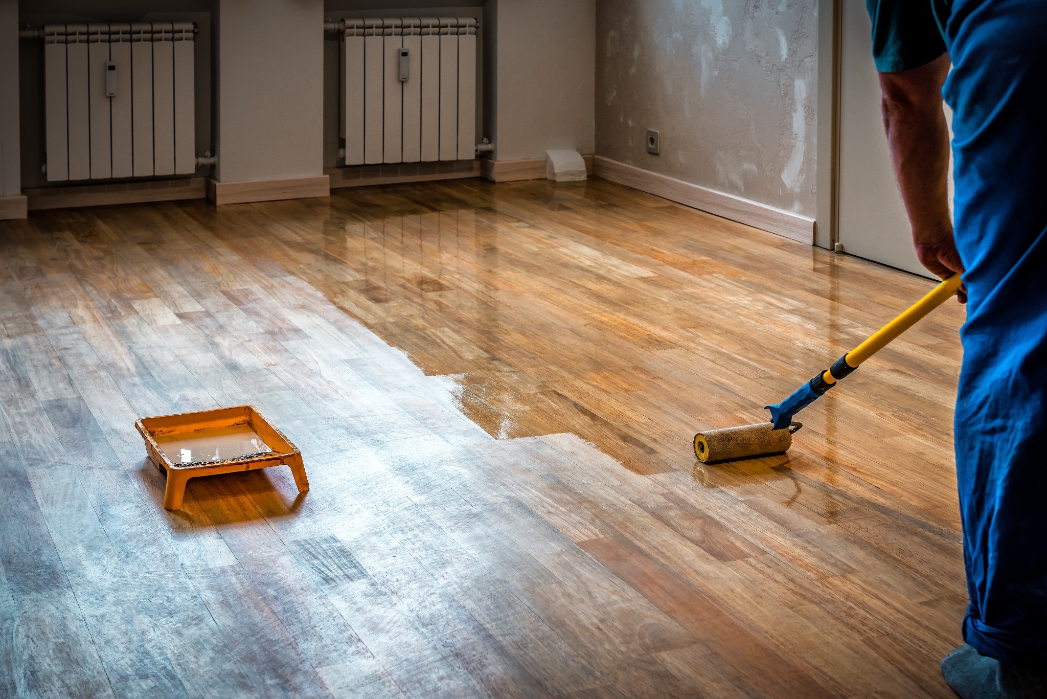 Hardwood Floor Refinishing in Southwark – technician applying clear lacquer with a roller to an oak hardwood plank floor, transforming the sanded boards into a smooth, glossy surface.