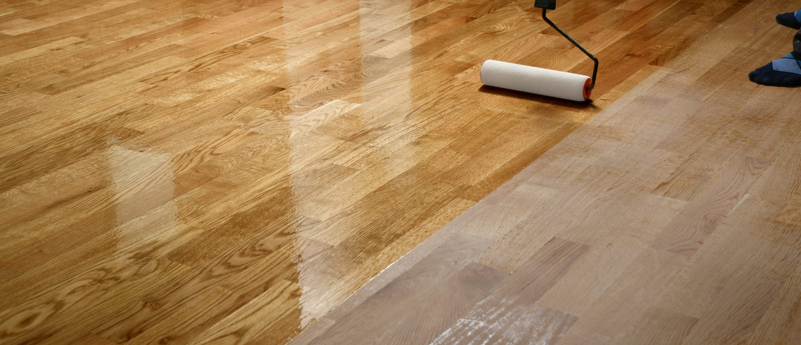 Hardwood Floor Refinishing in Southwark – close-up of an oak strip hardwood floor being sealed with a roller, showing the contrast between freshly lacquered boards and the sanded, unfinished timber.