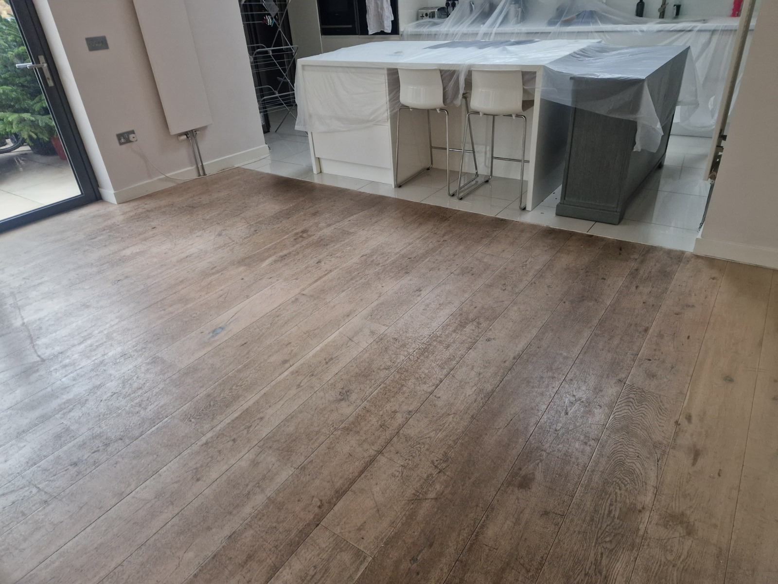 Hardwood Floor Refinishing in Southwark – worn oak wide plank hardwood floor in an open-plan kitchen-diner, showing dull, scratched boards before restoration.